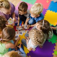Group of kindergarten kids sitting closely on a floor together with teacher, providing group work. Children learning to cooperate while solving tasks.